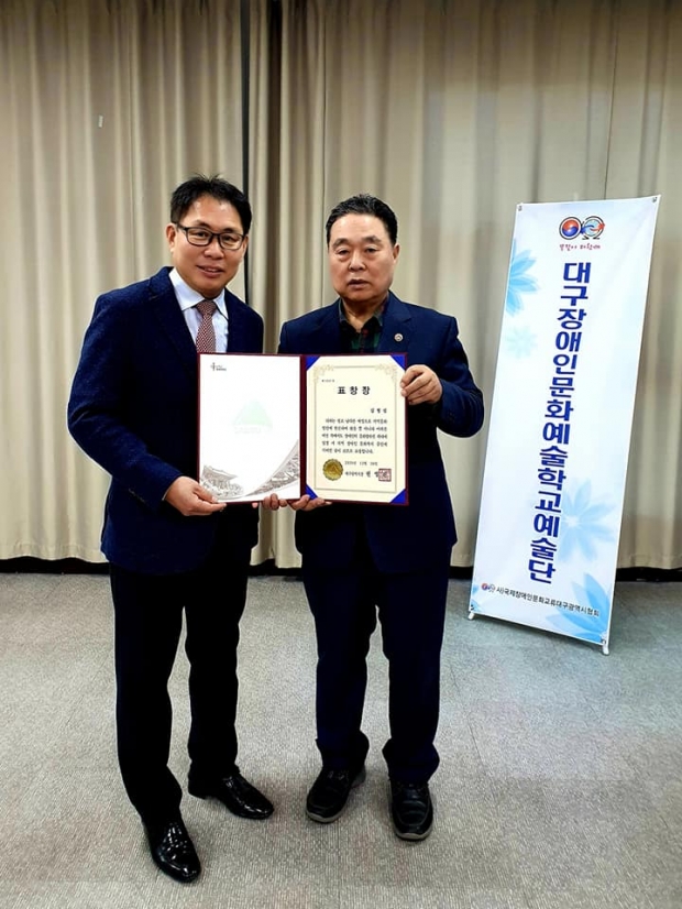 ▲김형섭 대구천사후원회 회장이 국제장애인문화교류협회장 정덕주 회장으로부터 대리로 권영진 대구시장 표창장을 수여하는 모습이다.
