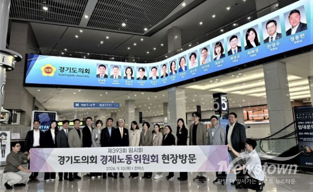 경기도의회 경제노동위원회가 10일 고양시 킨텍스를 방문한 가운데, 실내 상단 대형 안내 화면에 방문 의원들의 얼굴과 이름이 개인별로 게시돼 있다. 아래에서는 위원들과 관계자들이 현장방문 현수막을 들고 기념촬영을 하고 있다. /경기도의회 <br>